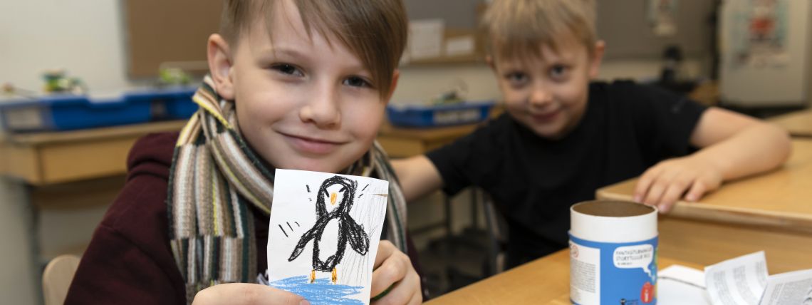 A boy is showing a drawing of a penguin. 